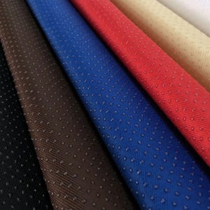 May include: Close-up of fabric swatches in various colors, including black, brown, blue, red, beige, and white. The fabric has a textured, dotted surface.
