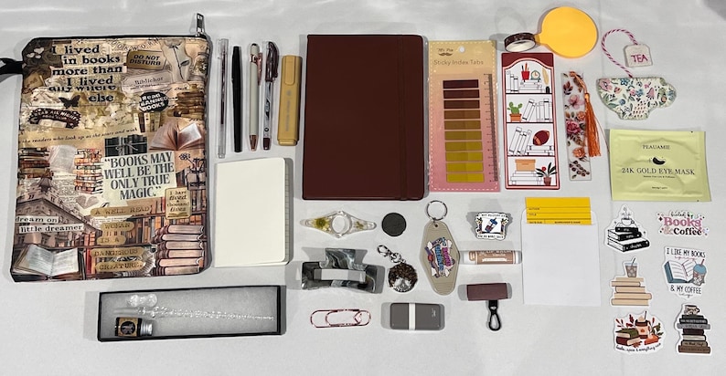 May include: A collection of stationery items including a book-themed zippered pouch, a dark red notebook, a white notepad, several pens, a highlighter, sticky index tabs, a bookmark, a glass dip pen with ink, stickers, and various small accessories.