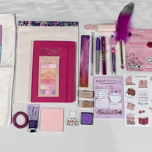 May include: A collection of stationery and book-themed items including a white tote bag with book tropes, a pink notebook, a spiral-bound Flower World coloring book, a glass cup, pens, a purple feather pen, stickers, sticky notes, and a small tube of lotion.