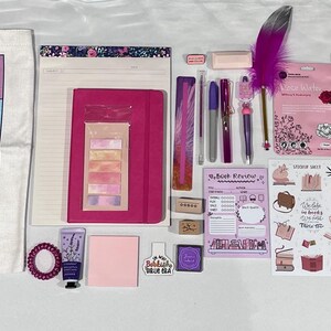 May include: A collection of stationery and book-themed items including a white tote bag with the text Book Lovers The Tropes Tour, a pink notebook, a spiral-bound Flower World coloring book, pens, a purple feather pen, stickers, and a glass jar.