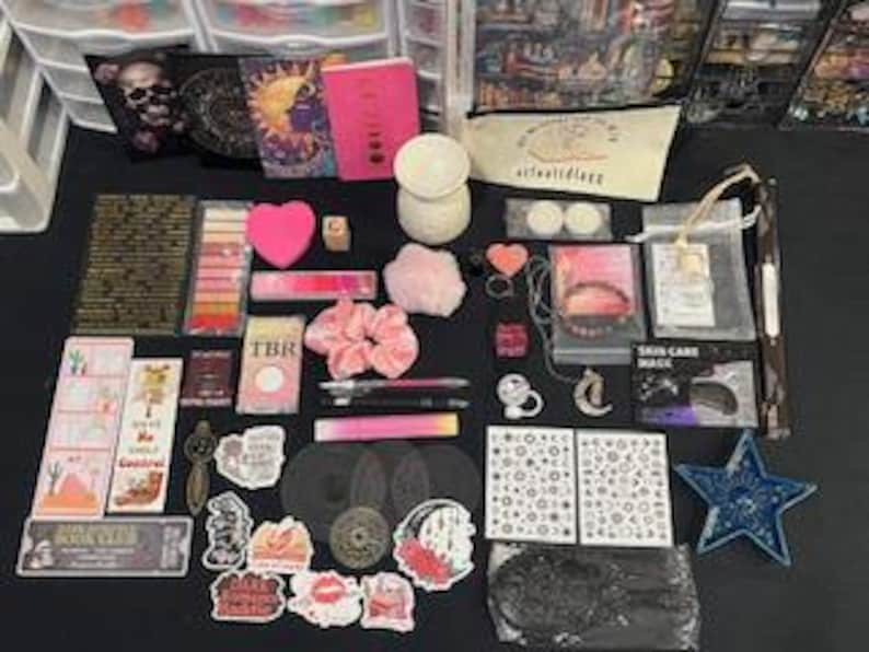 May include: A collection of stationery and lifestyle items including a pink notebook, a white wax warmer, various stickers, bookmarks, a pink scrunchie, a star-shaped dish, a small mirror, pens, and a canvas pouch with the text artfullyegg printed on it.