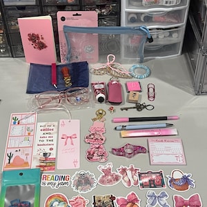 Peut inclure: Une collection de papeterie et d'accessoires comprenant un carnet rose, une pochette en filet bleu, des lunettes roses, un sceau à cire, des marque-pages avec texte, divers autocollants avec des nœuds, des livres, un squelette, des stylos et un bloc-notes.