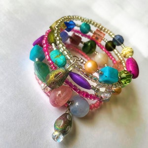 May include: Multi-colored beaded bracelet with a variety of beads, including turquoise, pink, green, and purple. The bracelet is made of several strands of beads wrapped around a silver wire.