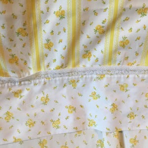 Peut inclure: Un tissu blanc orn&eacute; d'un motif de petites roses jaunes et de rayures verticales jaunes. Une bande horizontale de dentelle blanche s&eacute;pare la section ray&eacute;e d'une partie inf&eacute;rieure d&eacute;cor&eacute;e d'un imprim&eacute; floral jaune dispers&eacute;.