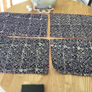 May include: Four blue and white patterned placemats with pink stitching. The placemats are made of a fabric material and have a geometric design.