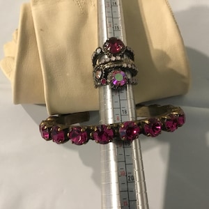May include: A selection of vintage jewellery, including a stack of rings with pink and clear gemstones, and a matching bracelet. The jewellery is displayed on a ring sizer, with a cream-coloured glove in the background.