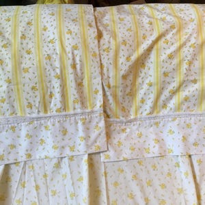 Peut inclure: Deux taies d'oreiller avec un fond blanc, un motif floral jaune et des rayures verticales jaunes. Chaque taie pr&eacute;sente un large ourlet agr&eacute;ment&eacute; d'une d&eacute;licate bordure en dentelle blanche le long de la couture s&eacute;parant l'ourlet du corps.