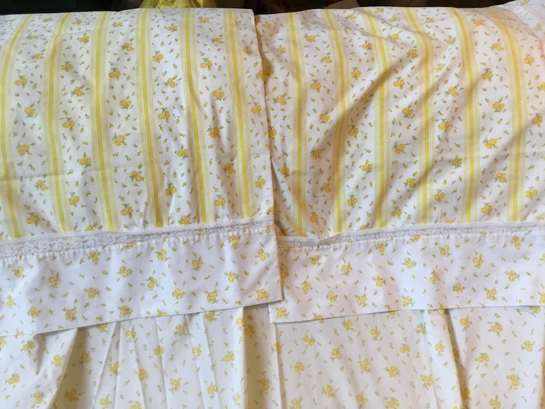 Peut inclure: Deux taies d'oreiller avec un fond blanc, un motif floral jaune et des rayures verticales jaunes. Chaque taie pr&eacute;sente un large ourlet agr&eacute;ment&eacute; d'une d&eacute;licate bordure en dentelle blanche le long de la couture s&eacute;parant l'ourlet du corps.