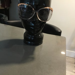 May include: A black mannequin head with a pair of large, oval-shaped sunglasses with a brown frame. The sunglasses have dark lenses.