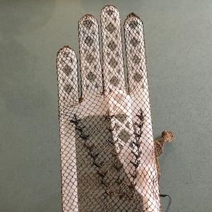 May include: A vintage, open-weave glove with a fishnet-like pattern. The glove features a brown net overlay on a white base, with a decorative design on the back of the hand. The fingers are individually defined, and the glove is likely made of a delicate material.