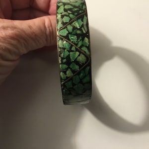 May include: A green and gold bangle bracelet with a mosaic design. The bracelet is made of metal and has a geometric pattern.