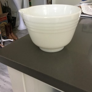 May include: Off-white mixing bowl with a pouring spout. The bowl has a rounded shape with horizontal ridges around the middle. It sits on a dark countertop.