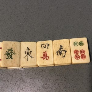 May include: A bracelet composed of five rectangular off-white tiles featuring engraved Chinese characters and circular symbols in black, red, and green ink. The tiles are connected by thin red elastic cords visible on the side of the first tile.