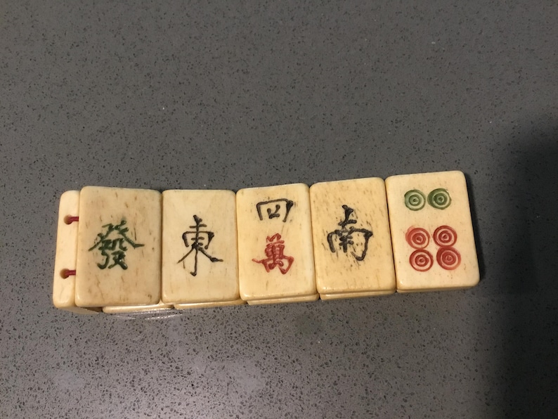 May include: A bracelet composed of five rectangular off-white tiles featuring engraved Chinese characters and circular symbols in black, red, and green ink. The tiles are connected by thin red elastic cords visible on the side of the first tile.