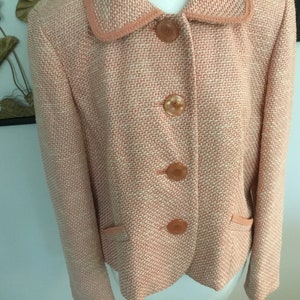 May include: A pink and white tweed blazer with a collar and four buttons. The blazer has two pockets on the front.