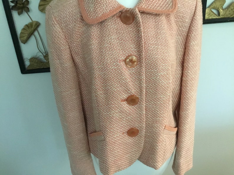 May include: A pink and white tweed blazer with a collar and four buttons. The blazer has two pockets on the front.