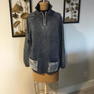 May include: A blue knitted sweater with a zippered collar and denim pockets. The sweater is on a mannequin.