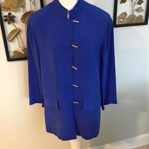 May include: A vibrant blue jacket with a mandarin collar and long sleeves. The jacket features gold-colored rectangular button closures down the front. The garment is displayed on a white mannequin, showcasing its tailored fit and design.