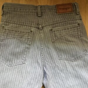 K&ouml;nnte beinhalten: Graue gestreifte Jeans mit einem braunen Leder-Patch, auf dem "Wrangler" auf der R&uuml;ckseite steht.
