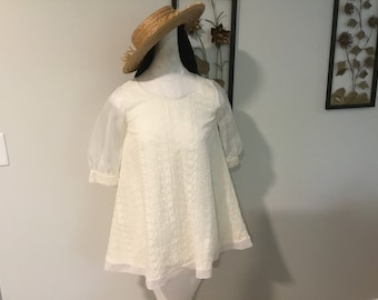 May include: A white, embroidered dress with a sheer overlay and a round neckline. The dress has a loose, flowing silhouette and is perfect for a summer occasion.