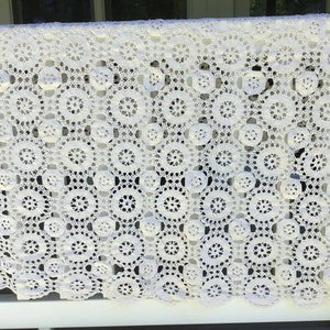 May include: White crocheted tablecloth with a repeating pattern of circles. The tablecloth is made of delicate, openwork lace.