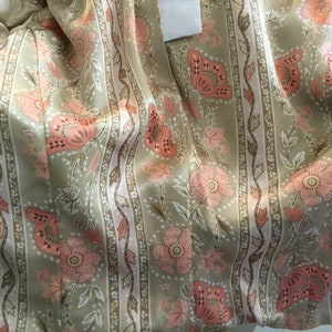 May include: Close-up of a beige fabric with a pink and brown floral pattern. The fabric has vertical stripes and a satin-like sheen.