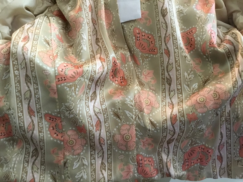 May include: Close-up of a beige fabric with a pink and brown floral pattern. The fabric has vertical stripes and a satin-like sheen.