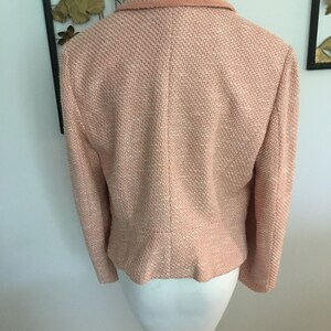 May include: A pink tweed blazer with a collar and long sleeves. The blazer is on a white mannequin.