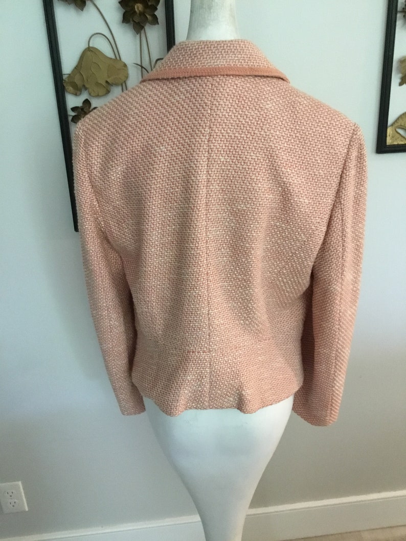 May include: A pink tweed blazer with a collar and long sleeves. The blazer is on a white mannequin.