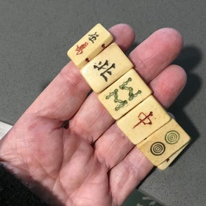 May include: A set of five rectangular off-white tiles with engraved markings. The tiles feature various black, red, and green symbols, including Chinese characters, a stylized green pattern, a red vertical line symbol, and two concentric circles.