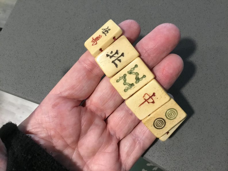 May include: A set of five rectangular off-white tiles with engraved markings. The tiles feature various black, red, and green symbols, including Chinese characters, a stylized green pattern, a red vertical line symbol, and two concentric circles.