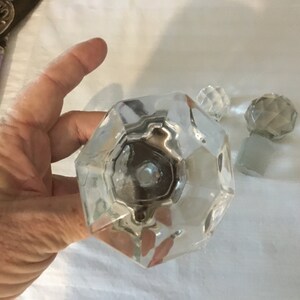 May include: Three clear glass bottle stoppers with a faceted design. The largest stopper is octagonal in shape.
