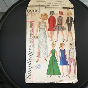 May include: Vintage Simplicity printed pattern 6208 for a doll, featuring illustrations of various doll outfits. The pattern includes the text "Doll One Size" and "Printed Pattern 50c". The cover shows several doll fashion designs.