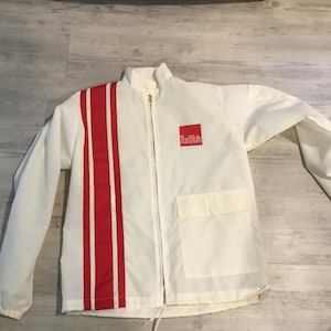 May include: White jacket with a red vertical stripe on the left side and a small red square logo on the right chest. The jacket has a full zipper, two pockets, and a drawstring at the bottom.