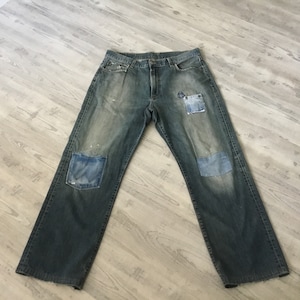 May include: A pair of blue denim jeans with multiple patches sewn on the legs. The jeans have a faded and distressed look.