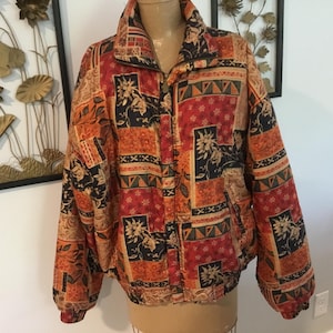 May include: A quilted jacket with a high collar and a zip closure. The jacket features a patchwork design in shades of red, orange, black, and beige, with floral and geometric patterns. The jacket has long sleeves and a relaxed fit.