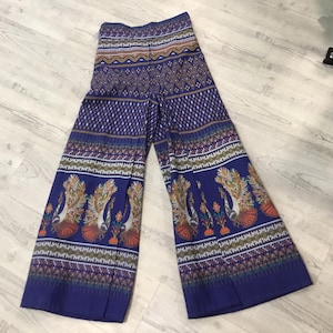 May include: Wide-leg trousers in a deep blue hue featuring a repeating geometric pattern at the waist and hem. The lower portion of the legs displays a vibrant print of multiple peacocks with orange and gold plumage standing among small floral motifs.