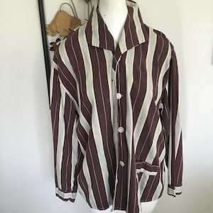 May include: A button-down shirt with vertical stripes in brown and off-white. The shirt has a collar, a chest pocket, and long sleeves with buttoned cuffs. The shirt is displayed on a white mannequin.