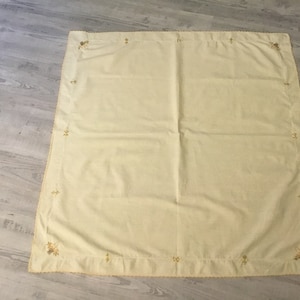 May include: A pale yellow tablecloth with a delicate embroidered border. The embroidery is in a darker yellow thread and features a floral design.