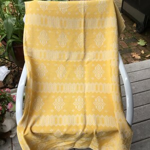 May include: A yellow throw blanket with a white geometric pattern. The blanket is draped over a white chair.