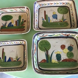 May include: Set of four ceramic baking dishes with colorful hand-painted designs featuring trees, cacti, and geometric patterns. The dishes have a white background with brown, green, blue, yellow, and red accents.