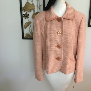 May include: A pink tweed blazer with a collared neckline and four button closures. The blazer has a fitted silhouette and a slightly cropped length.