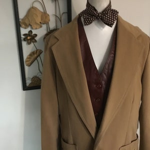 May include: A camel-colored long coat with a brown leather vest underneath. The coat has a wide lapel and a single button closure.
