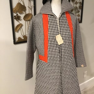 May include: A black and white gingham quilted coat with orange accents. The coat has a zipper closure and long sleeves.