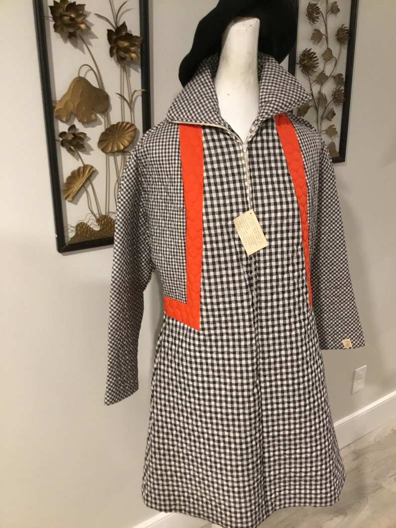 May include: A black and white gingham quilted coat with orange accents. The coat has a zipper closure and long sleeves.