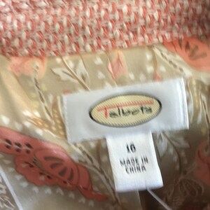 May include: A white label with the text "Talbots" in a red oval. The label is attached to a beige fabric with a pink floral pattern. The label also has the text "16" and "Made in China".