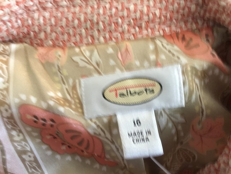 May include: A white label with the text "Talbots" in a red oval. The label is attached to a beige fabric with a pink floral pattern. The label also has the text "16" and "Made in China".