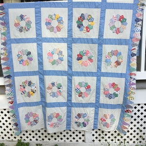 May include: A vintage quilt with a blue and white background and a patchwork design of colorful flowers. The quilt is made of various fabrics and has a scalloped edge.