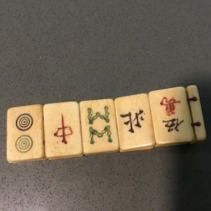 May include: A bracelet composed of five rectangular off-white tiles connected by thin brown cords. Each tile features distinct engraved markings, including concentric circles, a red vertical character, green symbols, and black Chinese characters.