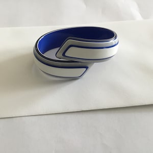 May include: A white and blue striped bangle bracelet with a geometric design. The bracelet is made of plastic and has a glossy finish.